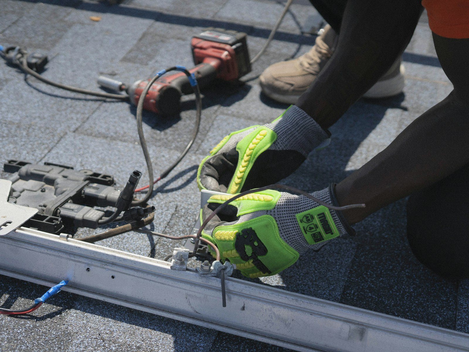 A roofer's gloved hands at work with a drill on an asphalt shingle roof