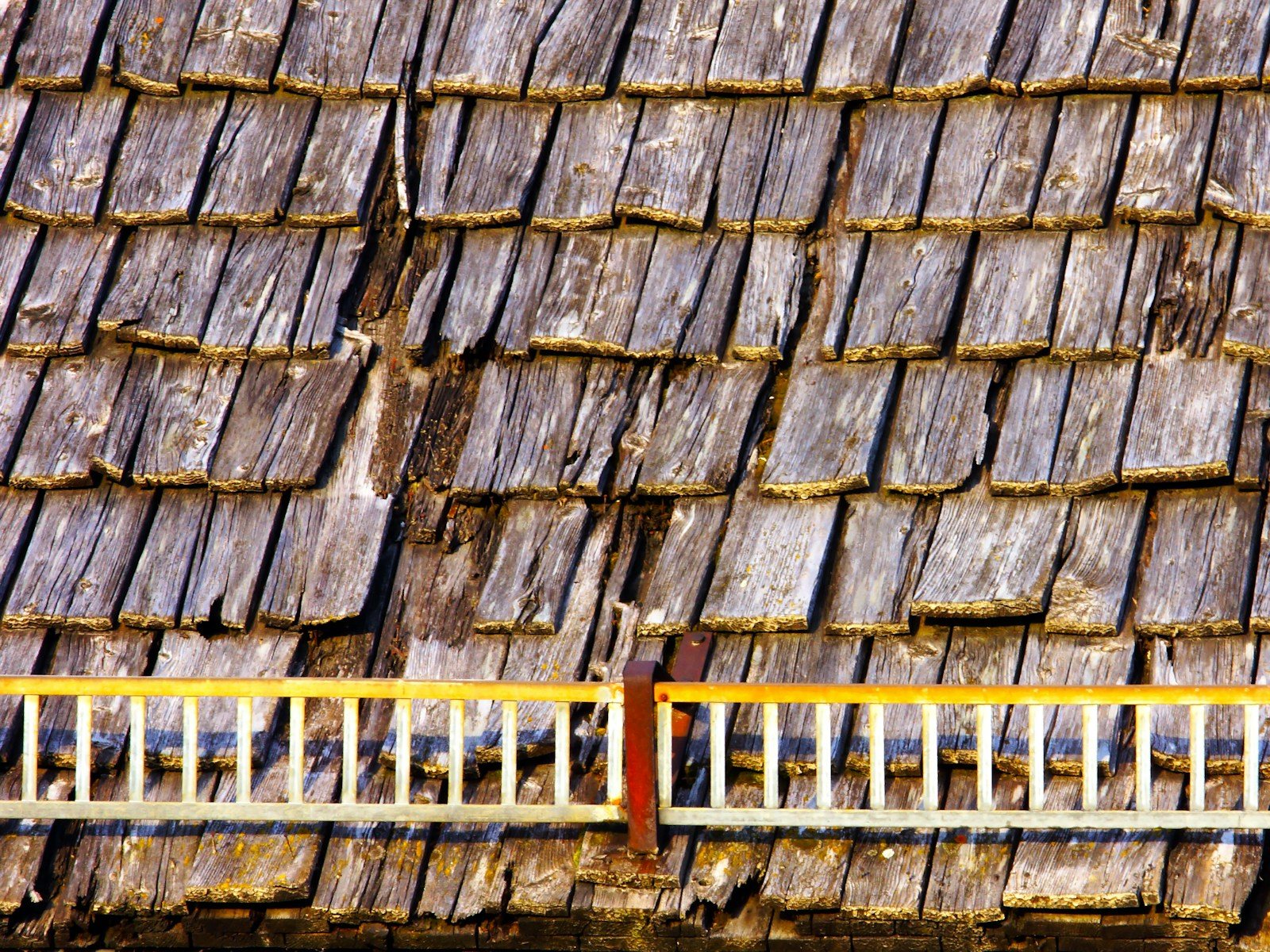 Old wood shingles on a roof with a ladder hooked over the ridge