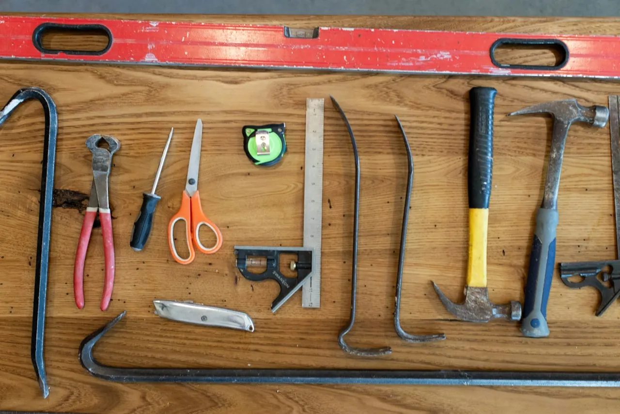 Hammers, a pry bar, a level and hand tools laid out on a board